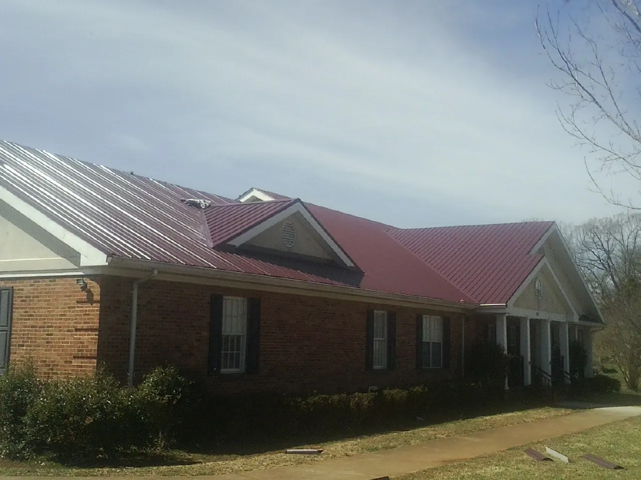 Red metal roof with gabled entries on a long brick building, from a Hail Damage Roof Repair job in Saint Charles