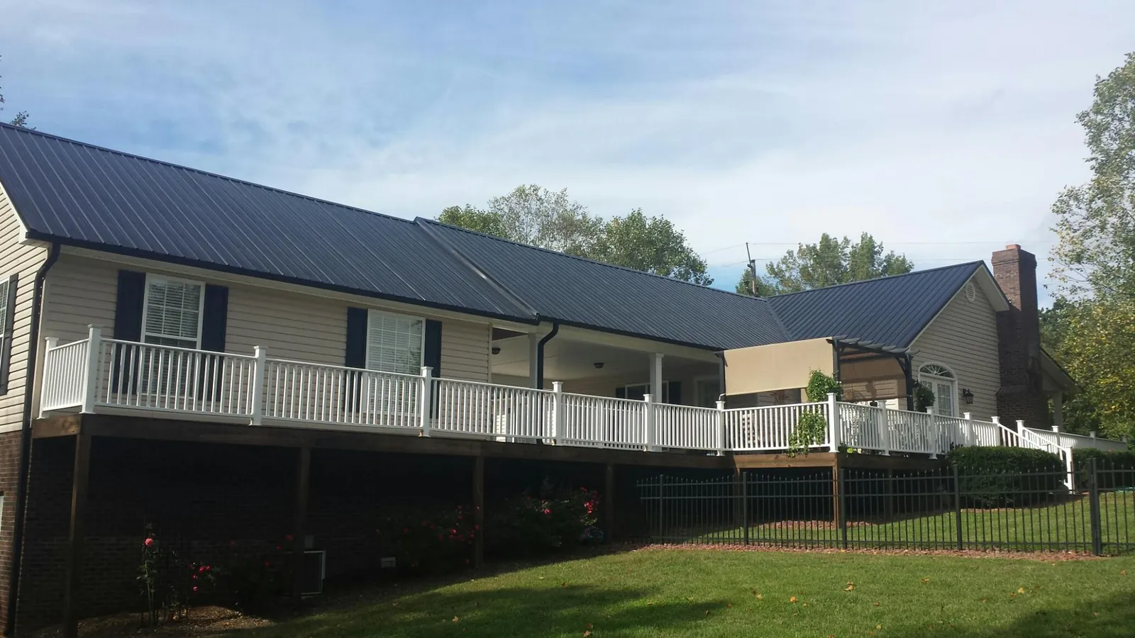 Black metal roof above a long white railed deck on a hillside home in Saint Charles